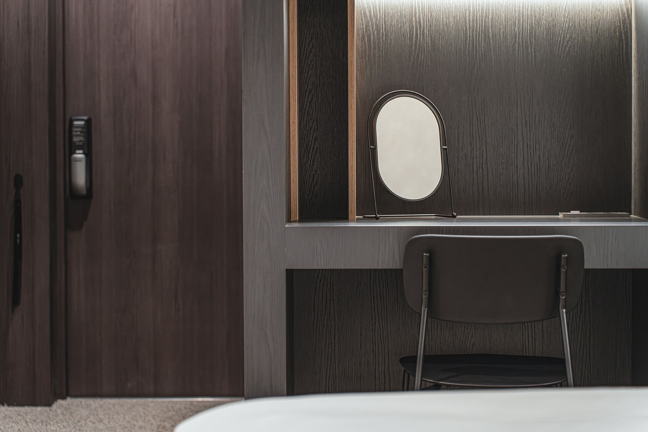 A room with a wooden wardrobe, a desk with a mirror, and a chair.