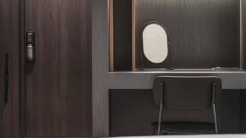 A room with a wooden wardrobe, a desk with a mirror, and a chair.