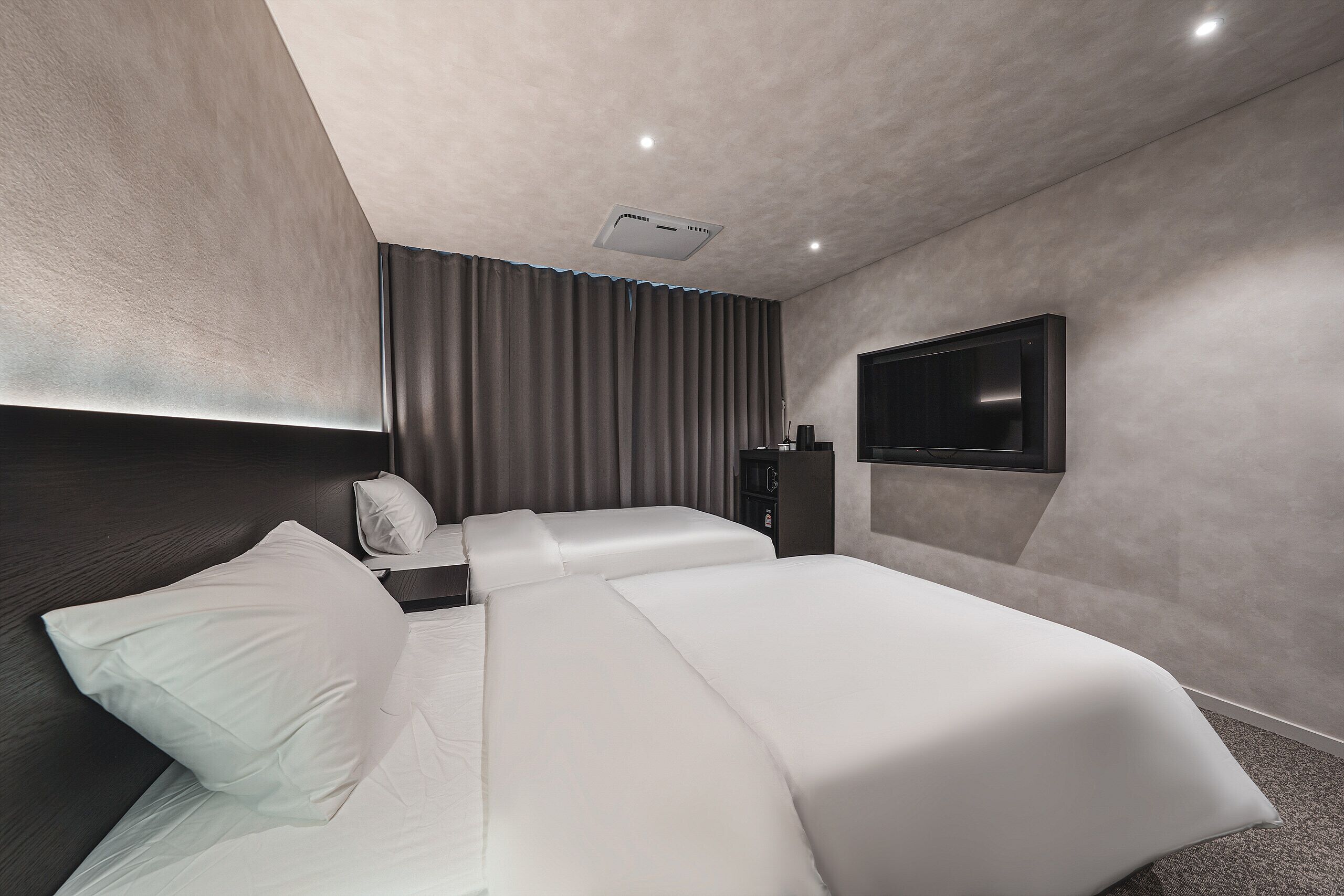 Una habitación de hotel moderna con una cama grande, un televisor de pantalla plana en la pared y un cabecero de madera oscura.