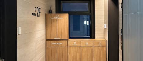 Un baño moderno con un mueble de madera para guardar toallas y artículos de aseo, un cesto para toallas usadas y cubos de basura para residuos generales, plásticos y vidrio.