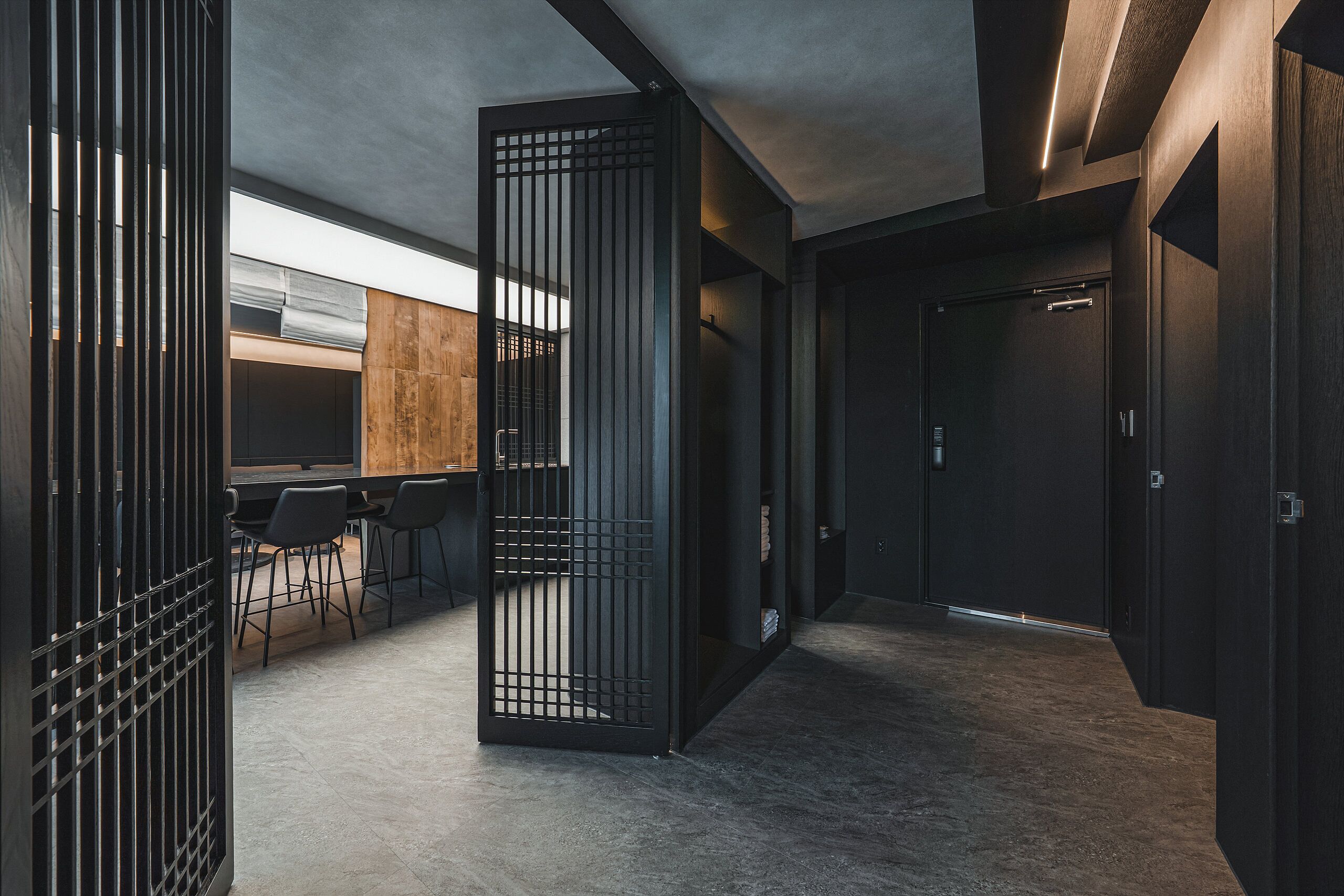 Un interior moderno con un pasillo oscuro, una pared de madera y una zona de estar con sillas.
