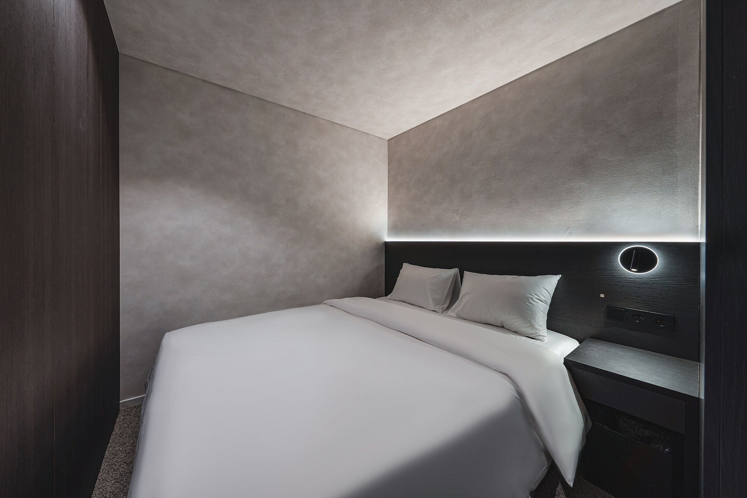 Una habitación de hotel moderna con una cama grande, un cabecero con luz circular y un armario de madera oscura.