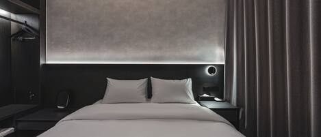Una habitación de hotel moderna con una cama grande, una mesita de noche, un armario y una ventana con cortinas.