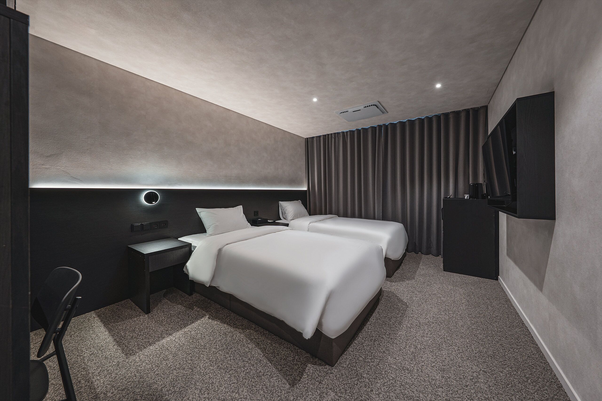 Una habitación de hotel moderna con dos camas, un escritorio, una silla, un televisor de pantalla plana y un amplio ventanal con cortinas.