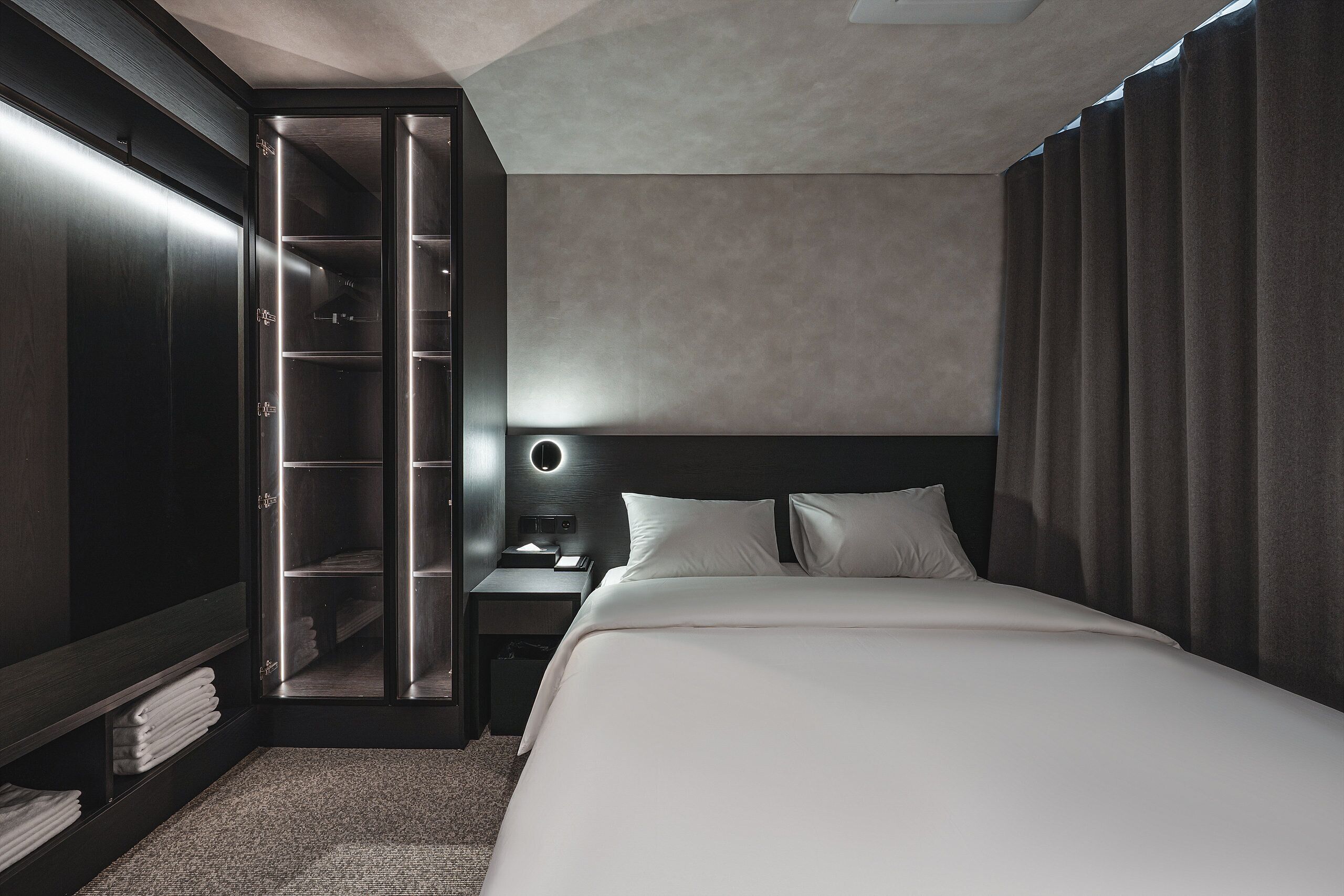 Ein modernes Hotelzimmer mit einem großen Bett, einem begehbaren Kleiderschrank und einem Nachttisch mit Lampe.