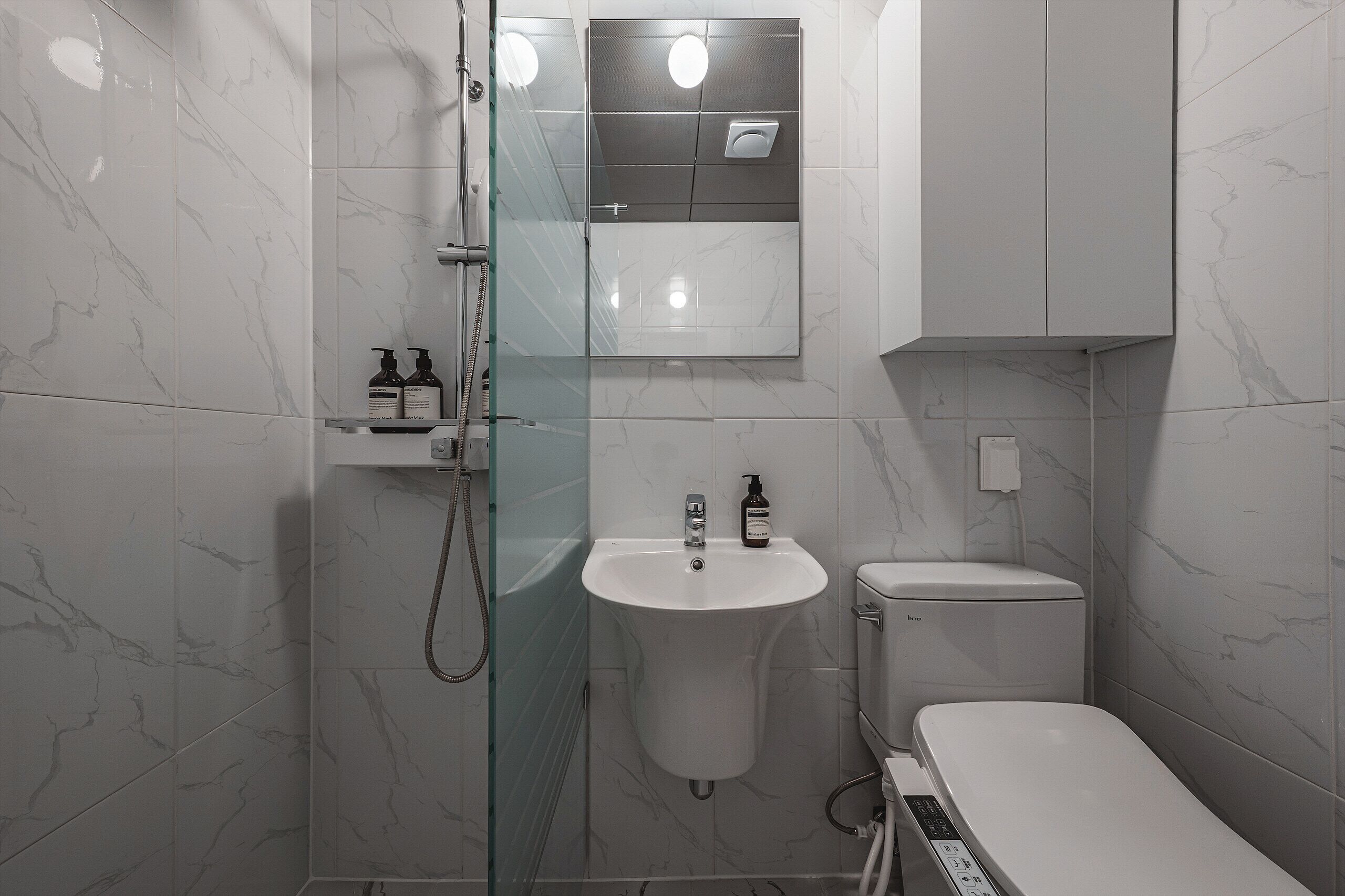 A modern bathroom with a glass-enclosed shower, a pedestal sink, and a toilet.