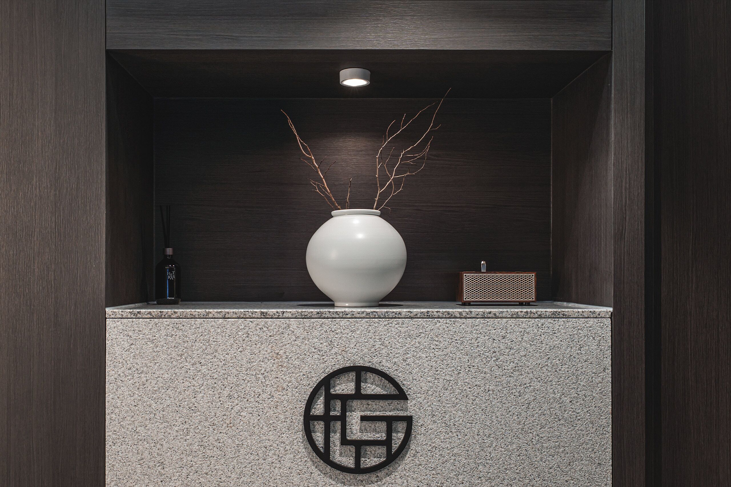 Un intérieur moderne avec un mur en bois foncé, un vase blanc orné de branches et une petite radio posée sur un comptoir en granit.