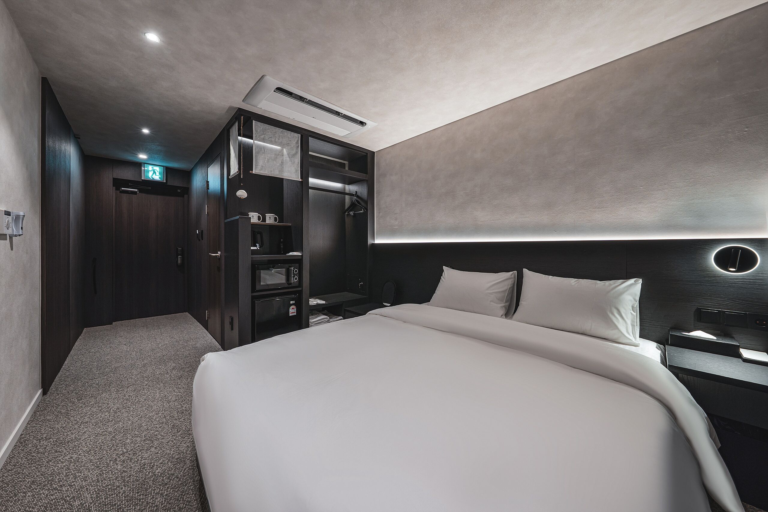 Una habitación de hotel moderna con una cama grande, un vestidor, un escritorio con silla y una mesita de noche.