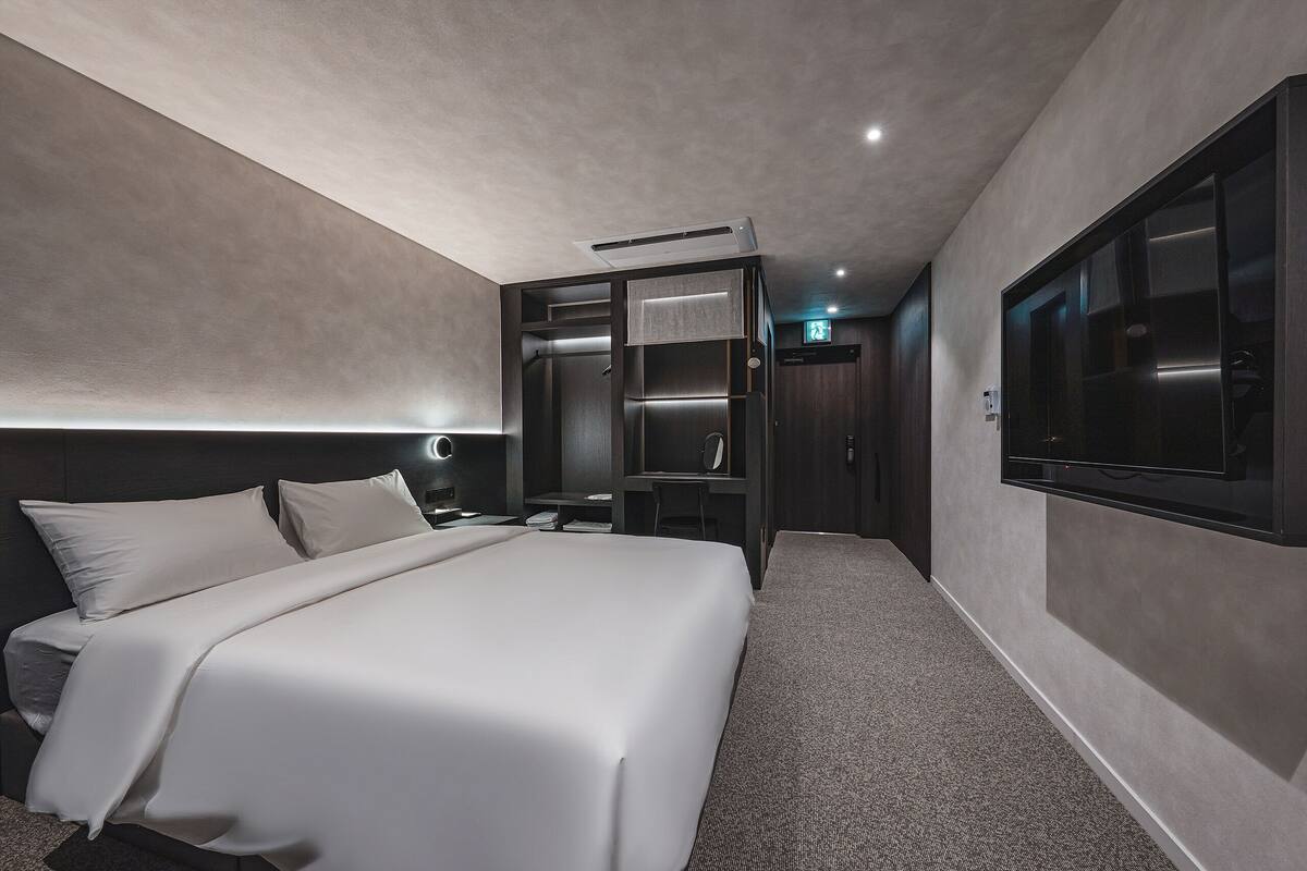 A modern hotel room with a large bed, built-in closet, bedside table, and a TV mounted on the wall.