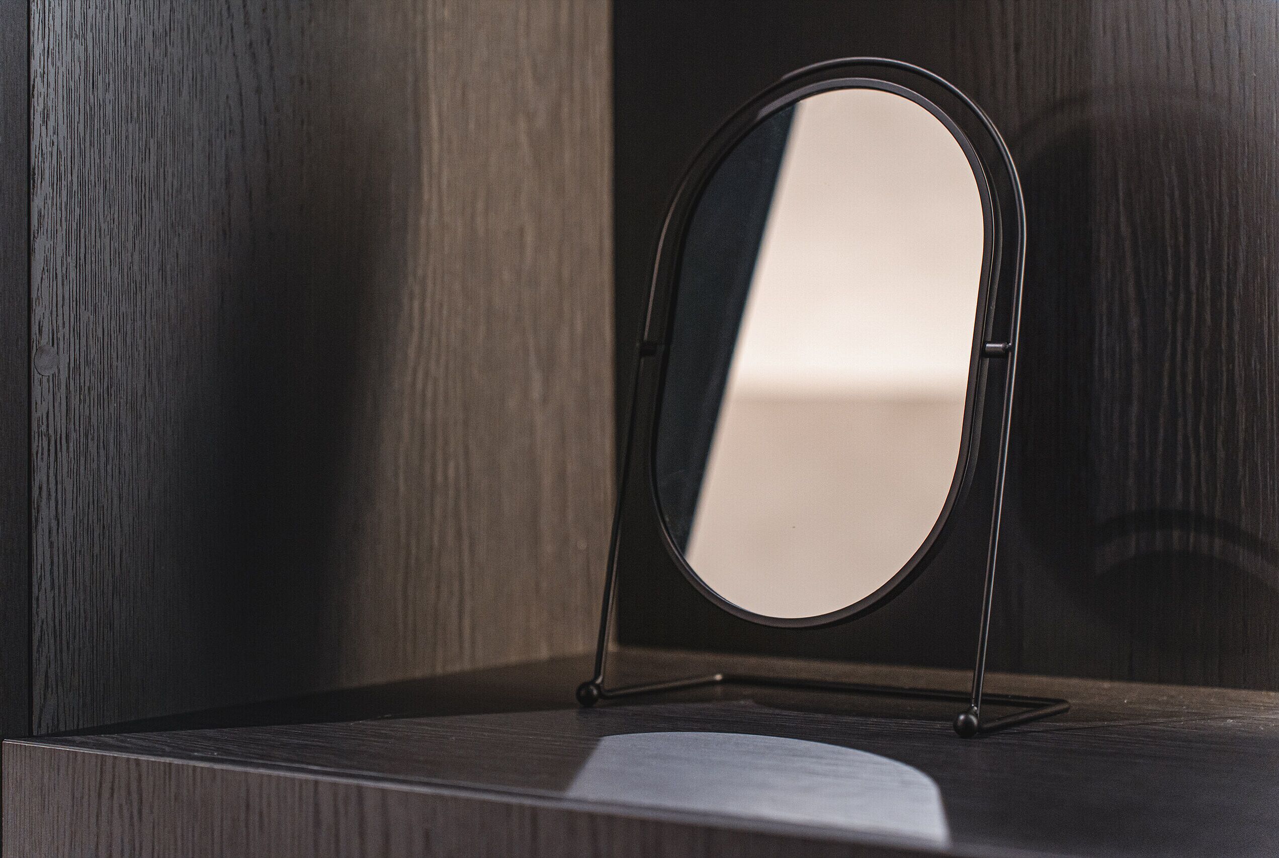 A round mirror on a stand against a wooden wall.