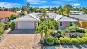 A residential property with a garage, a paved driveway, and a landscaped garden with palm trees and shrubs.