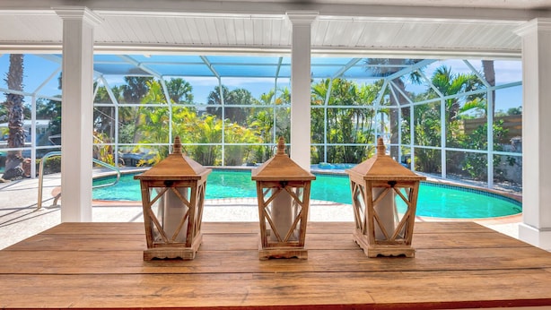 A pool area with three wooden lanterns on a wooden deck, surrounded by a glass enclosure with a view of a pool and tropical vegetation.