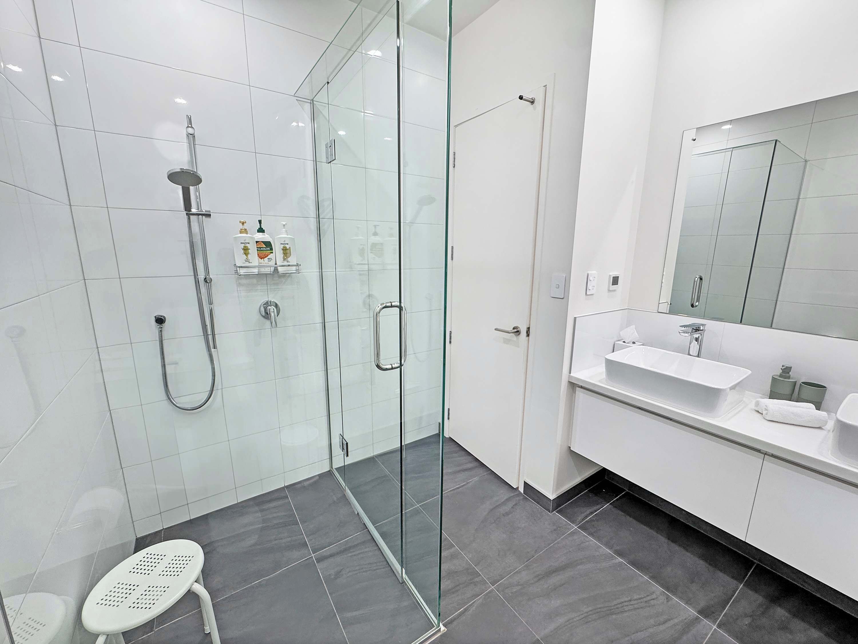 A modern bathroom with a glass-enclosed shower, a white sink, and a large mirror.