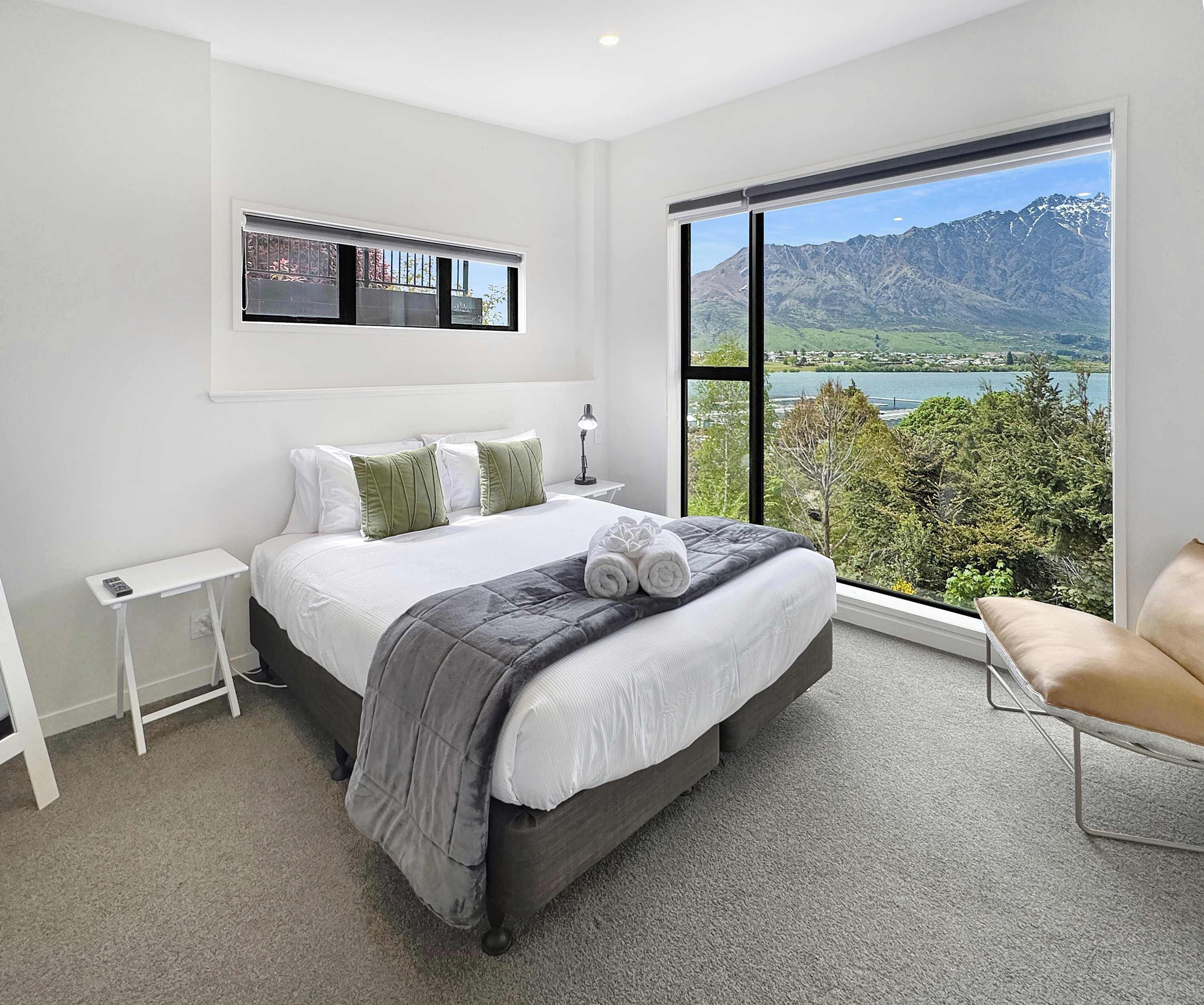 Ein modernes Schlafzimmer mit einem großen Bett, einem Nachttisch, einem Sessel und Blick auf Berge und einen See.