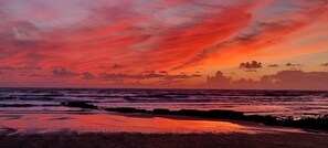 Un atardecer sobre el océano con olas y una costa rocosa.