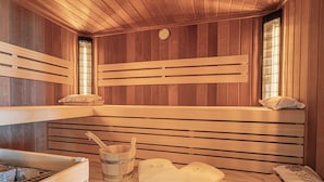 Un sauna avec des bancs en bois, un seau en bois, des serviettes et un radiateur.