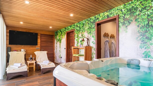 Une salle de spa dotée d’un bain à remous, d’un plafond en bois et d’un mur orné d’une fresque représentant un feuillage verdoyant.