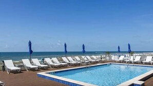 Ein Poolbereich mit Liegestühlen und Sonnenschirmen mit Blick auf das klare, blaue Meer.