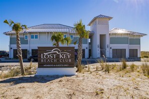 A beach club with a signboard, a modern building with a flat roof, and palm trees in the foreground. - 4BR Home Beach Access and Resort Pools (Pensacola)