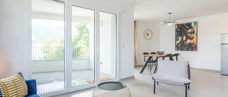 Ein modernes Wohnzimmer mit einem blauen Sofa, einem Essbereich mit Tisch und Stühlen sowie einer Küchenzeile mit Kühlschrank.