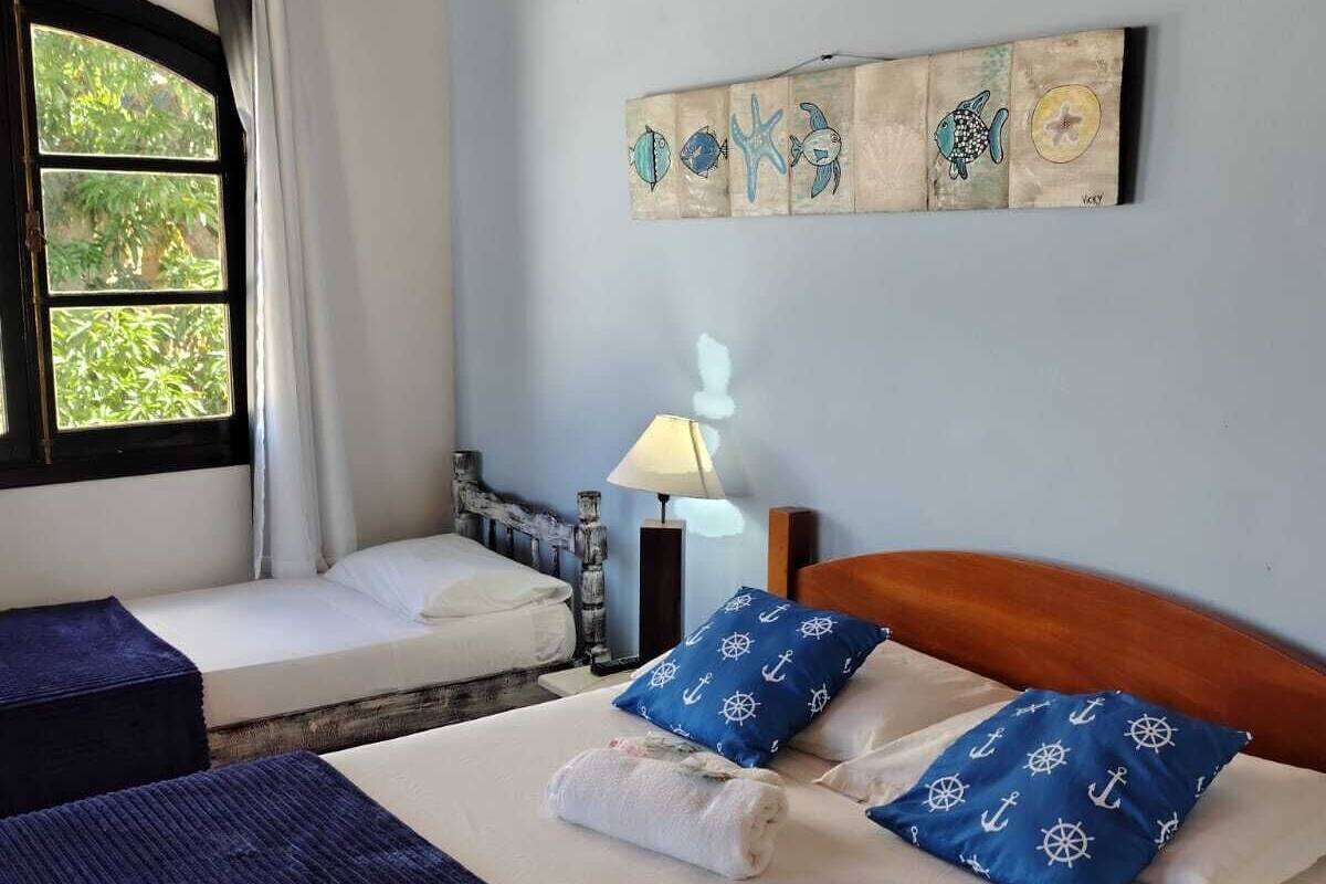 Ein Zimmer mit einem Bett, zwei Nachttischen, einer Lampe und einem fensterbelaubten Fenster.