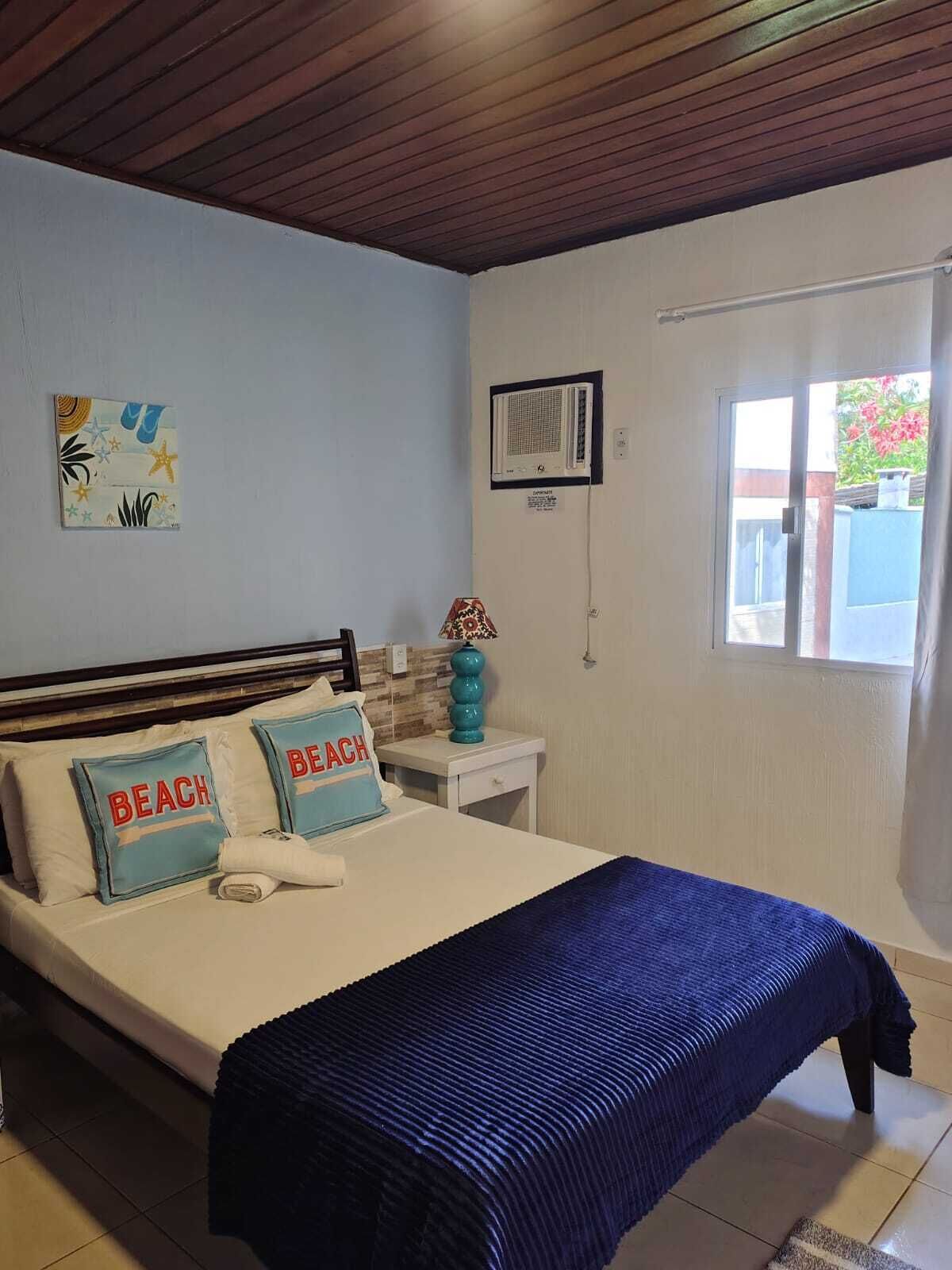 A bedroom with a bed, pillows, a nightstand, a window, and a wall-mounted air conditioner.