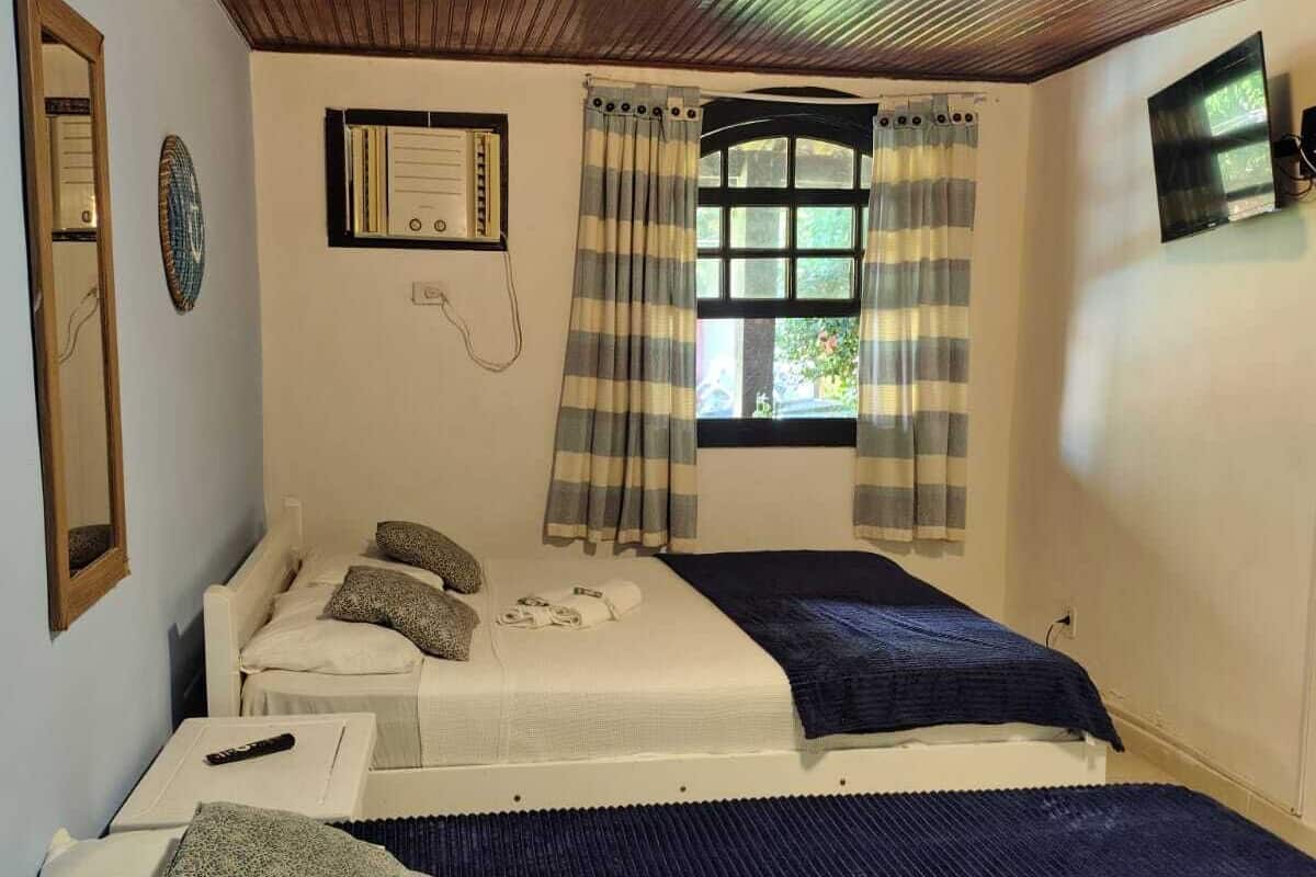 Ein Schlafzimmer mit zwei Betten, einem fensterbelaubten Fenster, einer Uhr und einem an der Wand befestigten Fernseher.