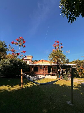 A house with a hammock in the yard, surrounded by trees and a clear sky. - Pousada bela casa geriba (Buzios)