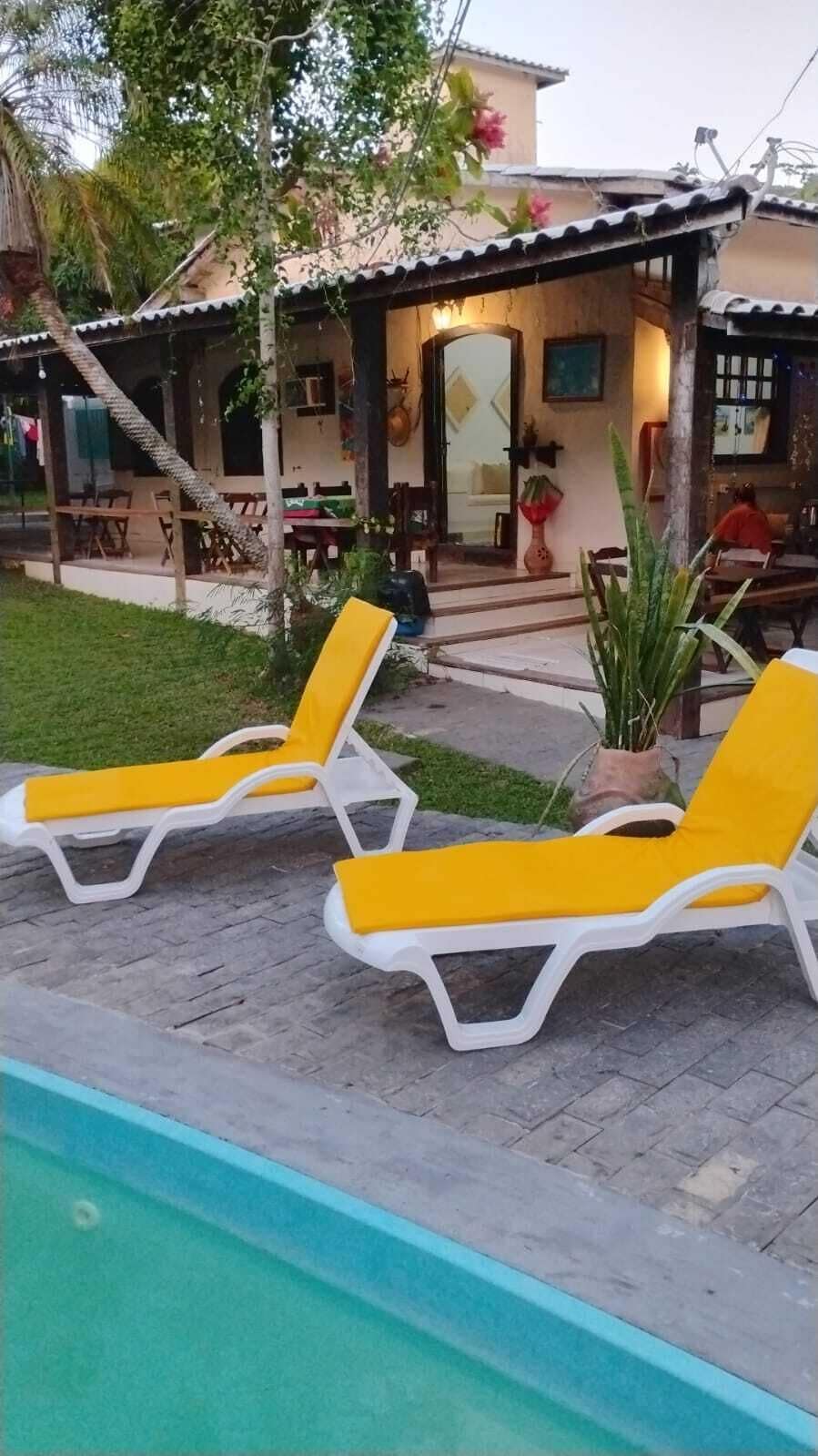 Une piscine entourée de deux chaises longues jaunes, avec un bâtiment à l’arrière-plan dont le toit est recouvert de tuiles.