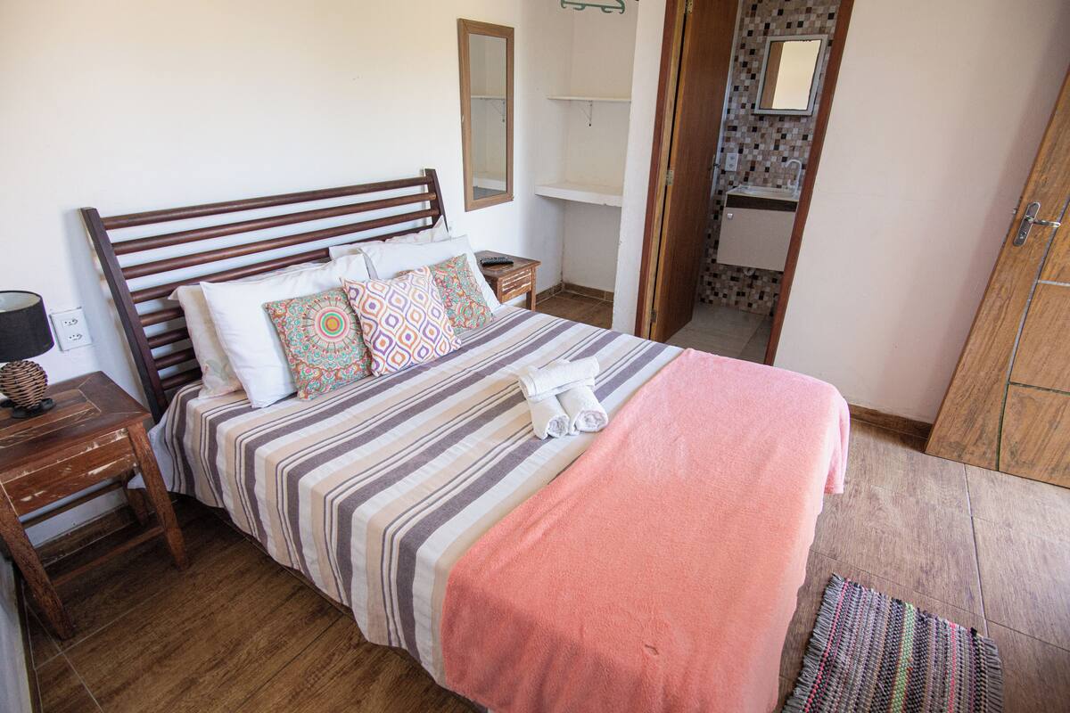 Ein Schlafzimmer mit einem hölzernen Bett, gestreifter Bettwäsche, einer rosafarbenen Decke und einem kleinen Nachttisch mit einer Lampe.