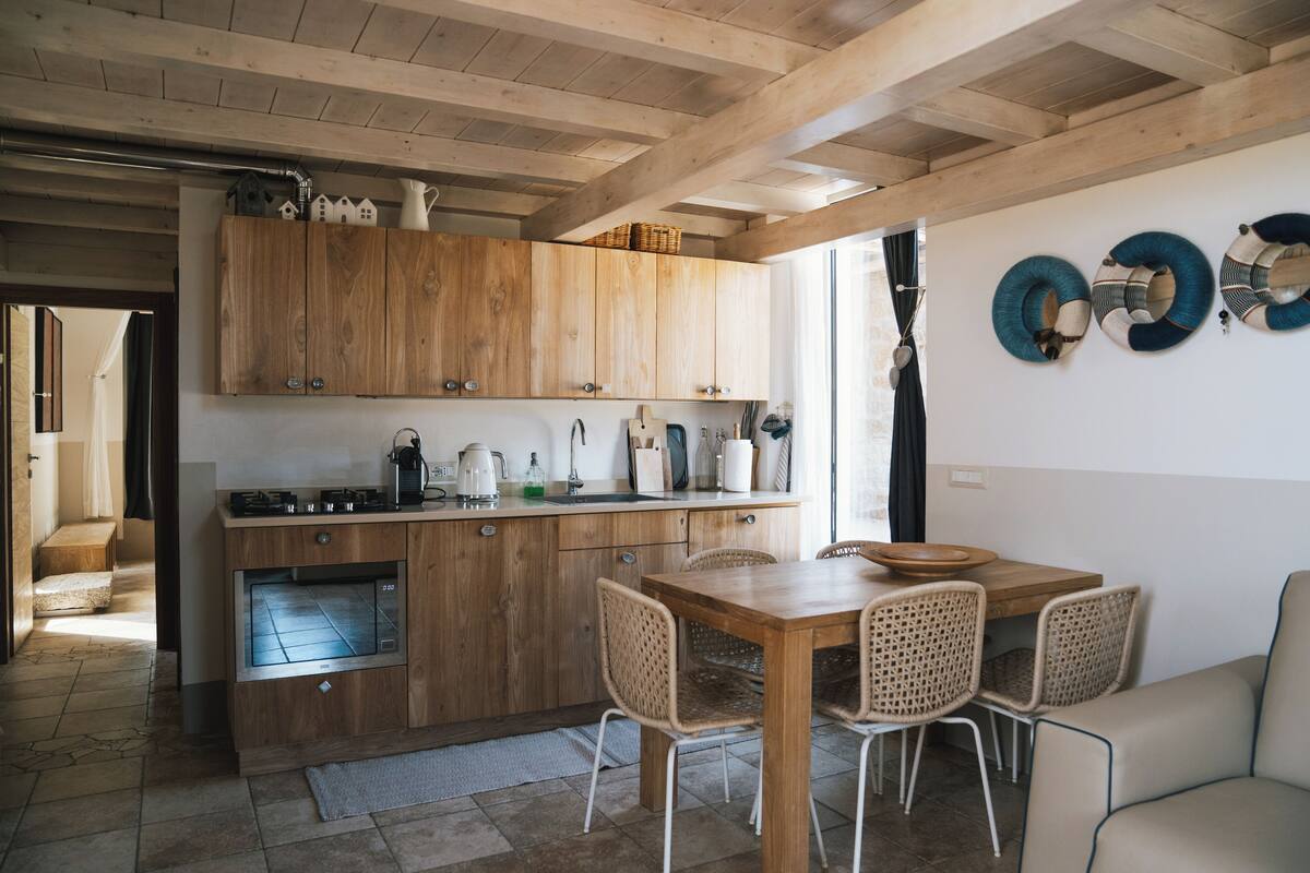 A kitchen with wooden cabinets, a dining table with chairs, and a window with curtains.