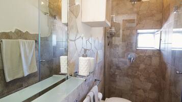 A bathroom with a glass shower enclosure, a white sink, and a toilet.