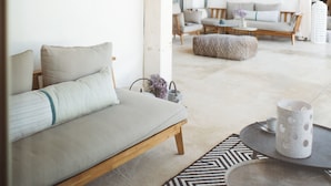 Un espacio habitable moderno y abierto con techo de madera, un sofá, una mesa redonda y una alfombra estampada.