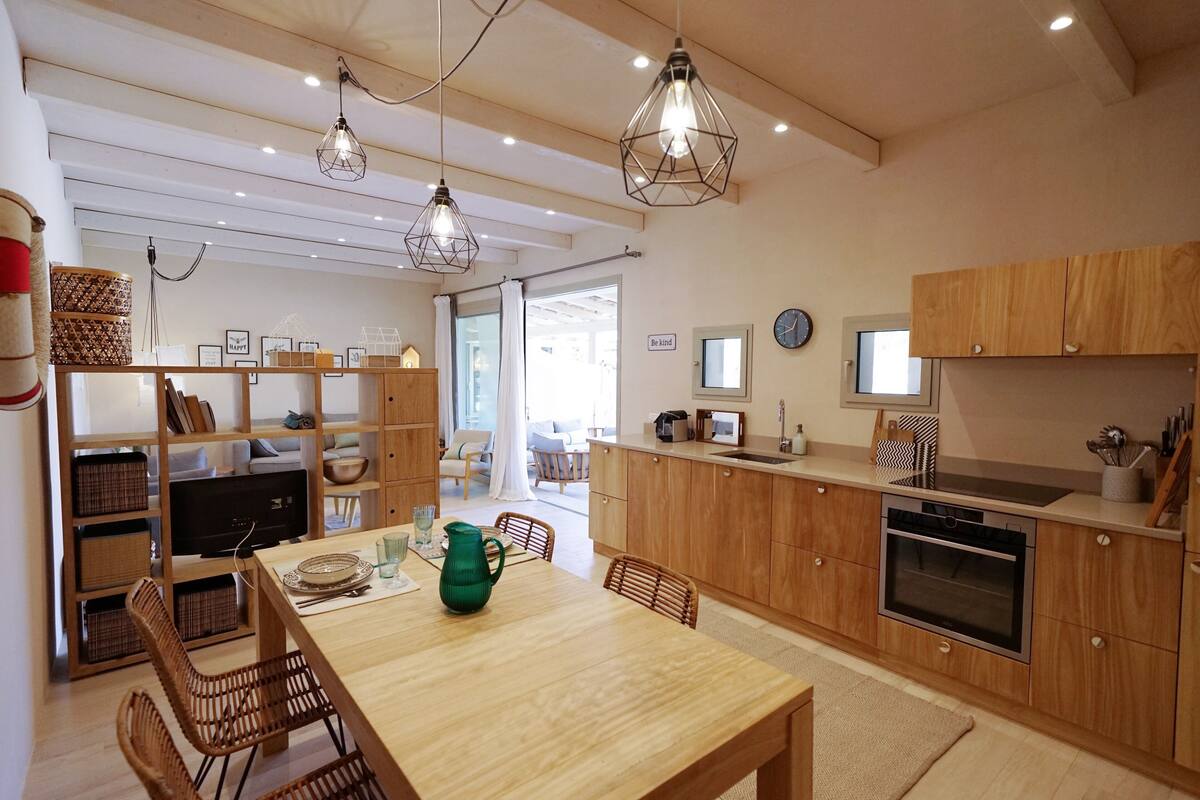 A modern kitchen with wooden cabinets, a dining table with chairs, and pendant lighting.