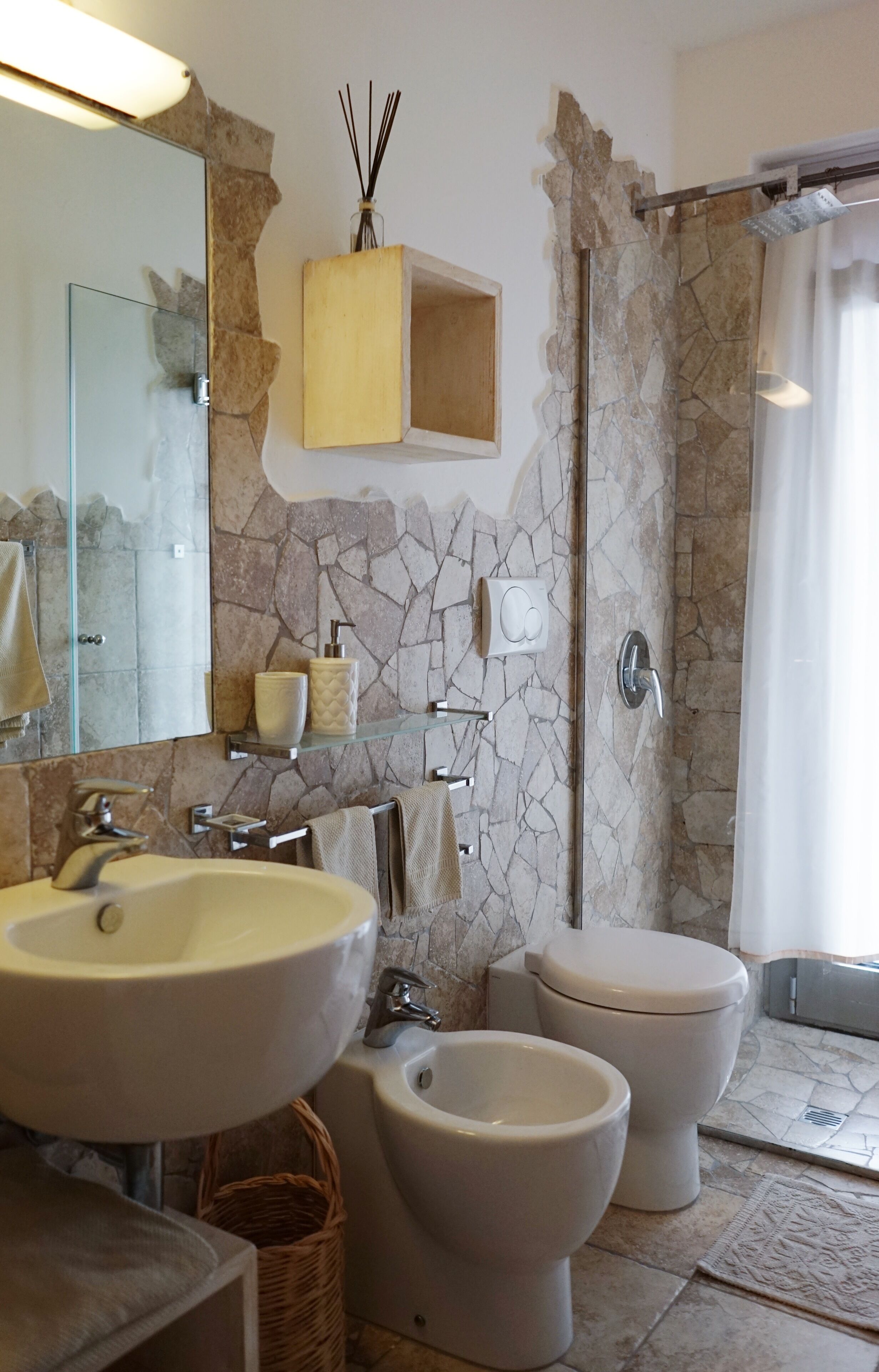 Une salle de bain avec un mur en pierre, un grand lavabo, deux toilettes et un espace douche.