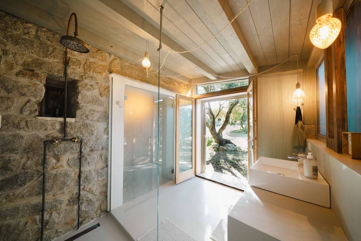 A modern bathroom with a stone wall, a glass door leading outside, and a white sink area.