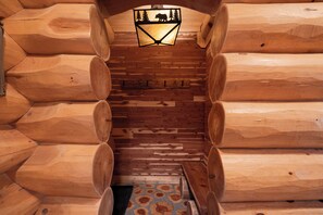Ein Holzblockhaus-Innenraum mit einer zentralen Treppe, Holzwänden und einer dekorativen Deckenleuchte.