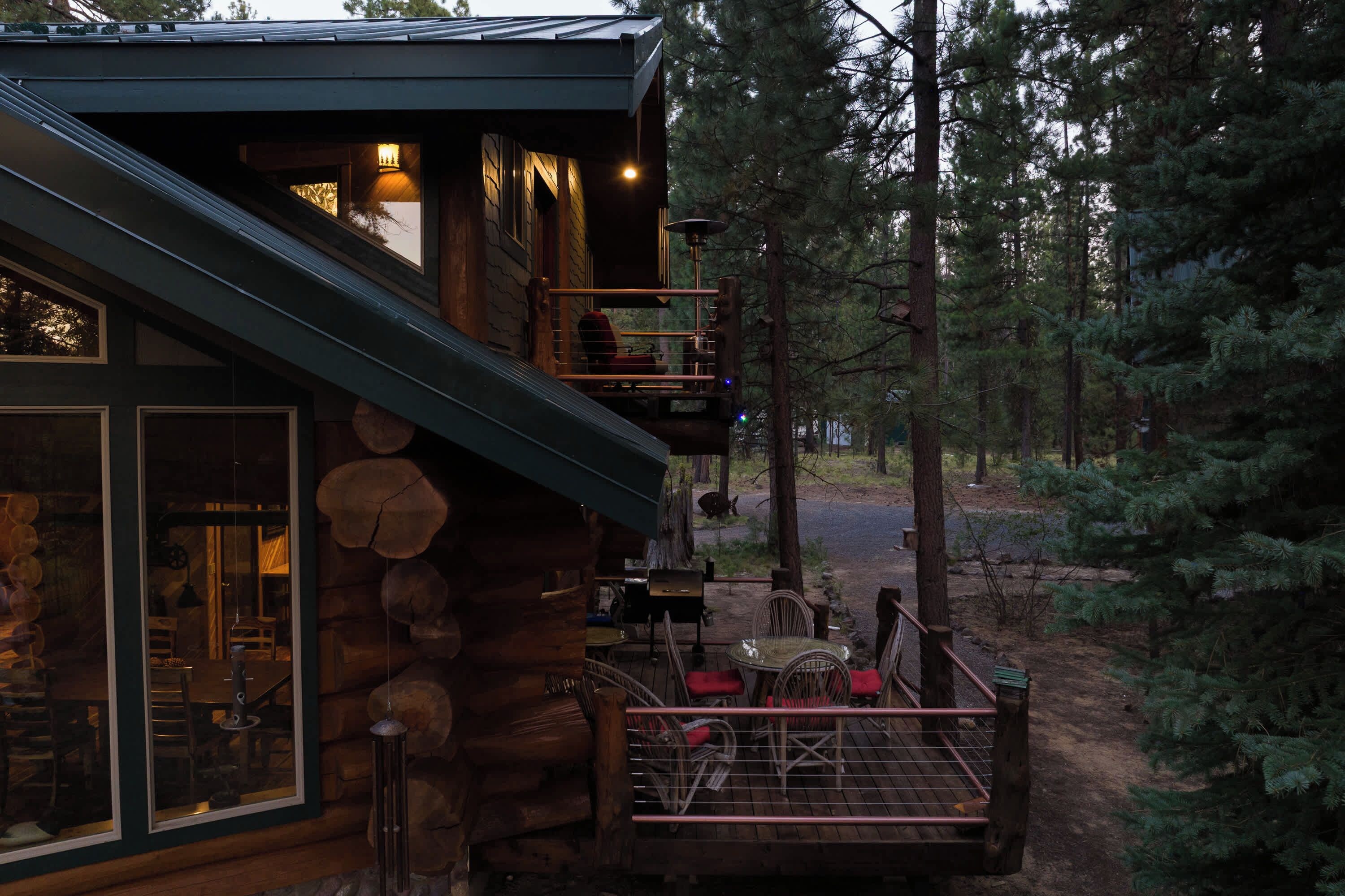 Une cabane en rondins dotée d’un balcon, d’un coin repas et offrant une vue sur la forêt.