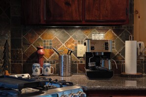 A kitchen with a coffee maker, two mugs, a knife block, and a stove.