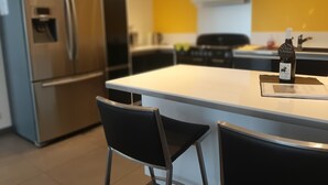 Une cuisine moderne dotée d’appareils électroménagers en acier inoxydable, d’un îlot central blanc et de tabourets de bar noirs.