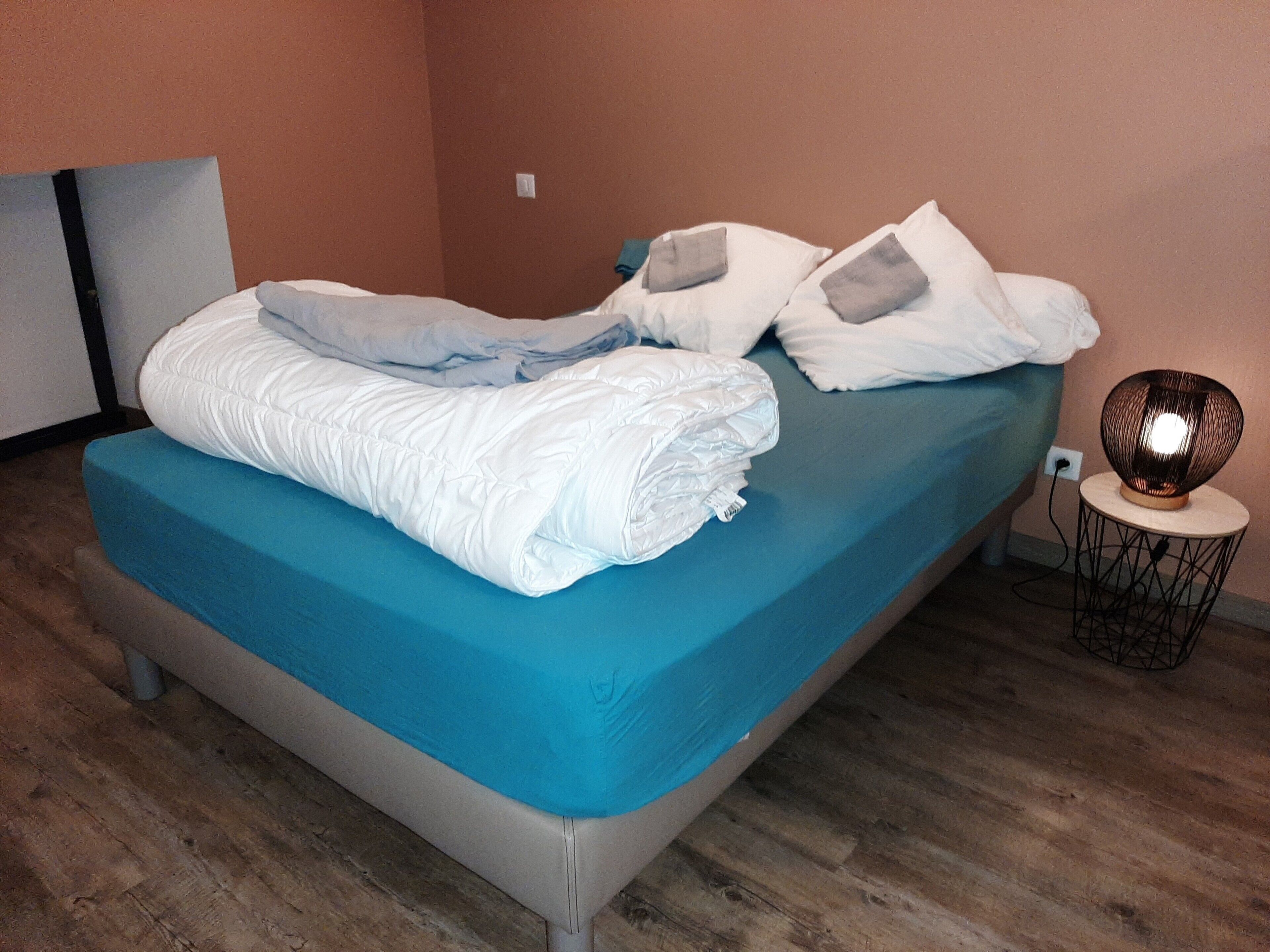 A neatly made bed with a blue mattress cover, white pillows, and a white duvet.