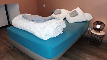 A neatly made bed with a blue mattress cover, white pillows, and a white duvet.