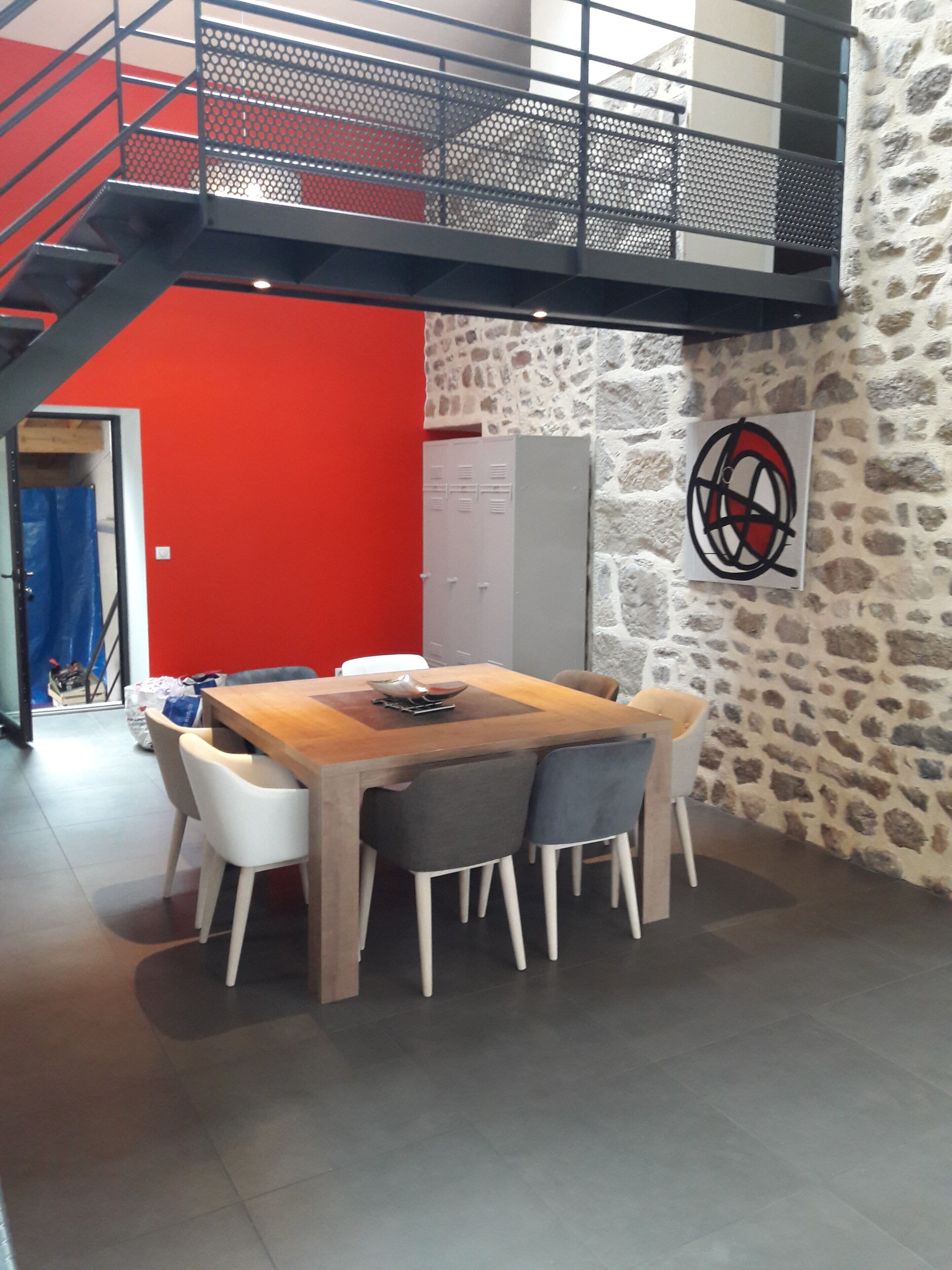A dining area with a wooden table and chairs, a staircase, and a stone wall.