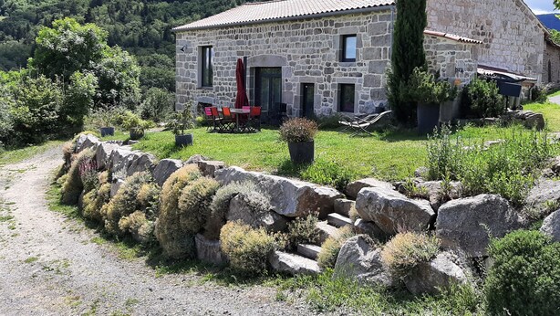 Un bâtiment en pierre avec un toit en tuiles, un chemin pavé et de la verdure tout autour.