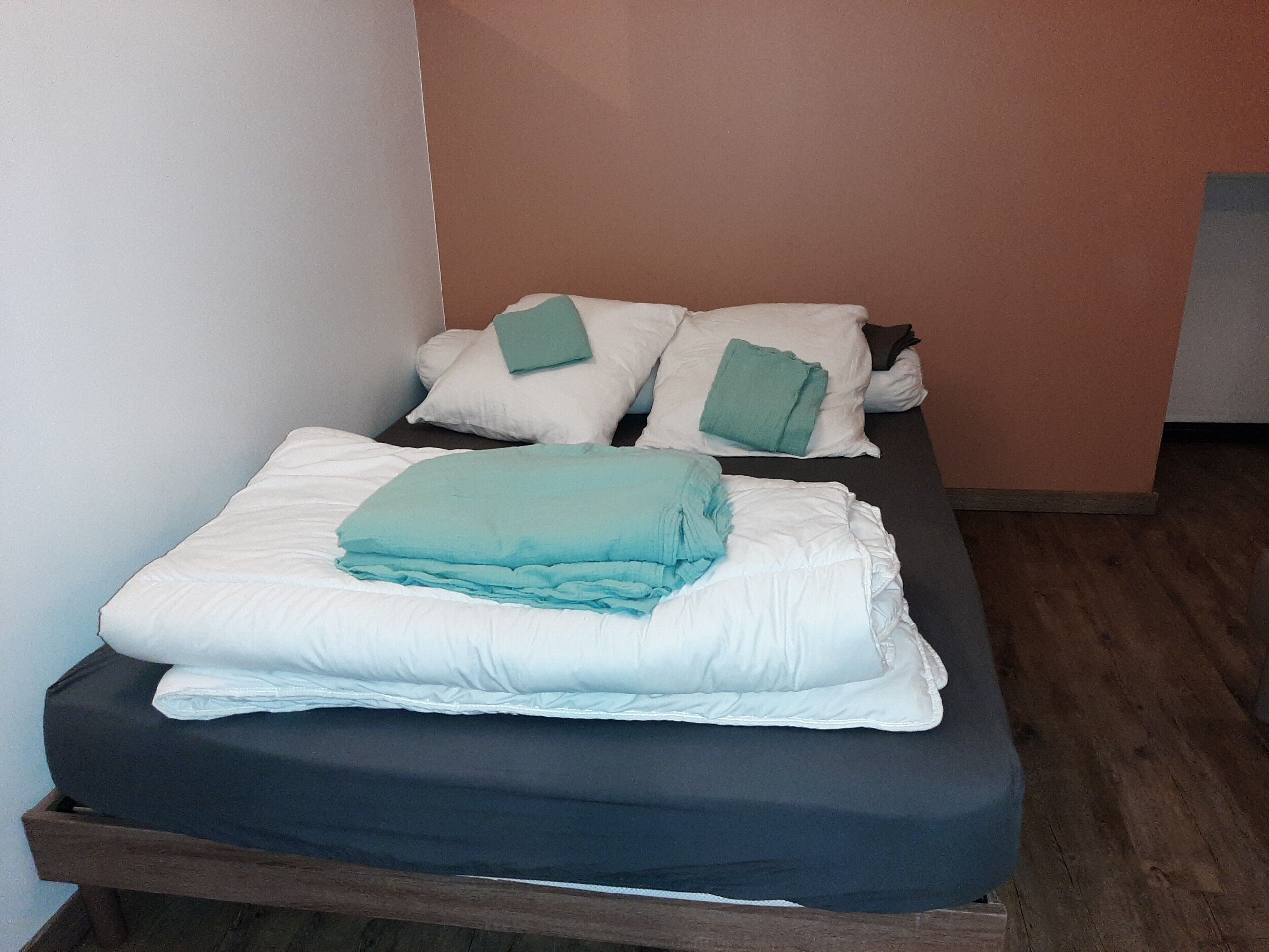 A single bed with a dark mattress and white pillows, a folded blanket, and a green pillow on top.