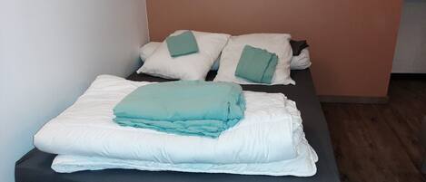 A single bed with a dark mattress and white pillows, a folded blanket, and a green pillow on top.