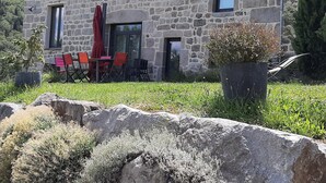 Un bâtiment en pierre doté d’une terrasse, de sièges en plein air et d’une grande plante en pot.