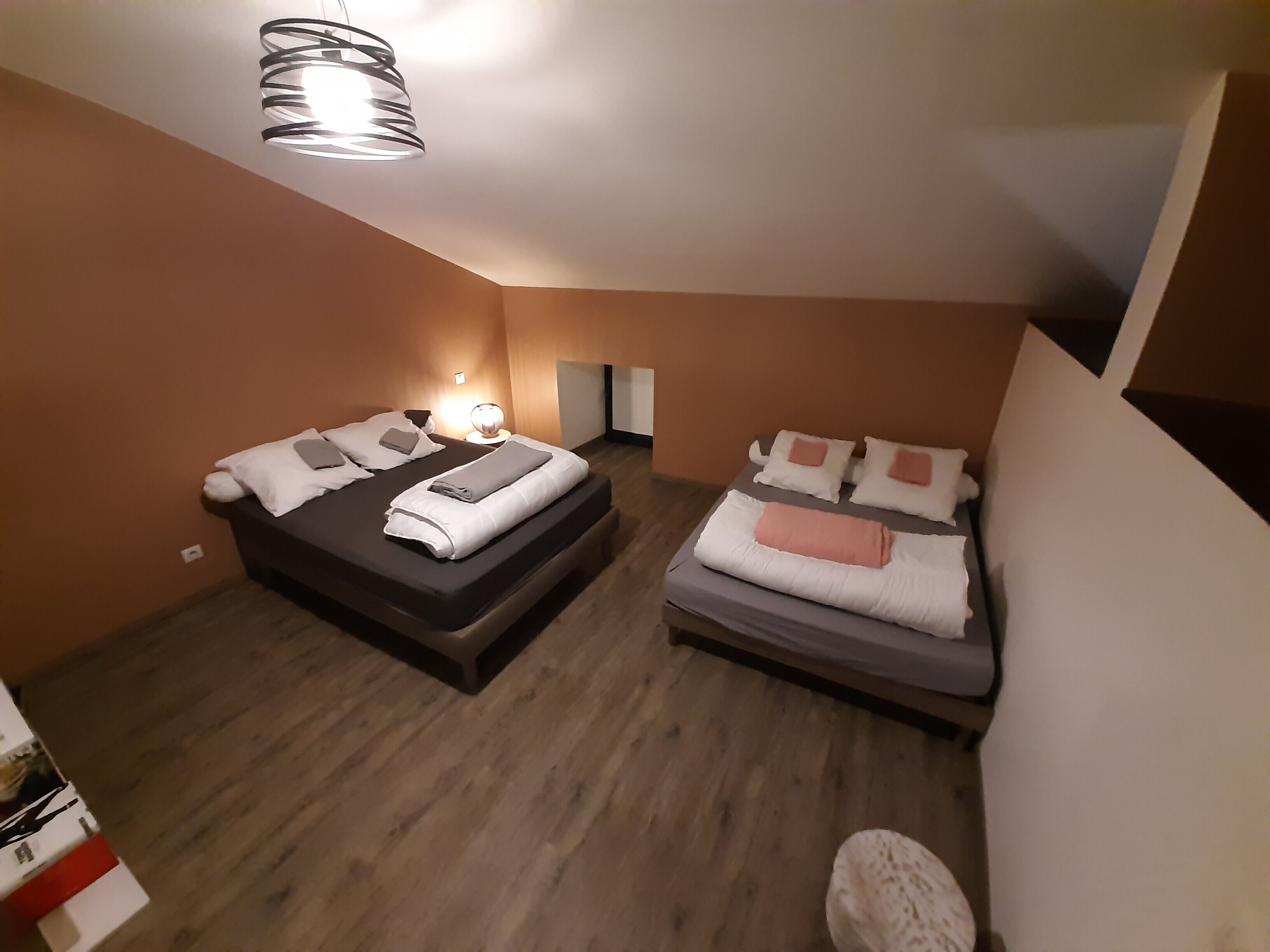 Una habitación de hotel con dos camas, una lámpara moderna y suelo de madera.