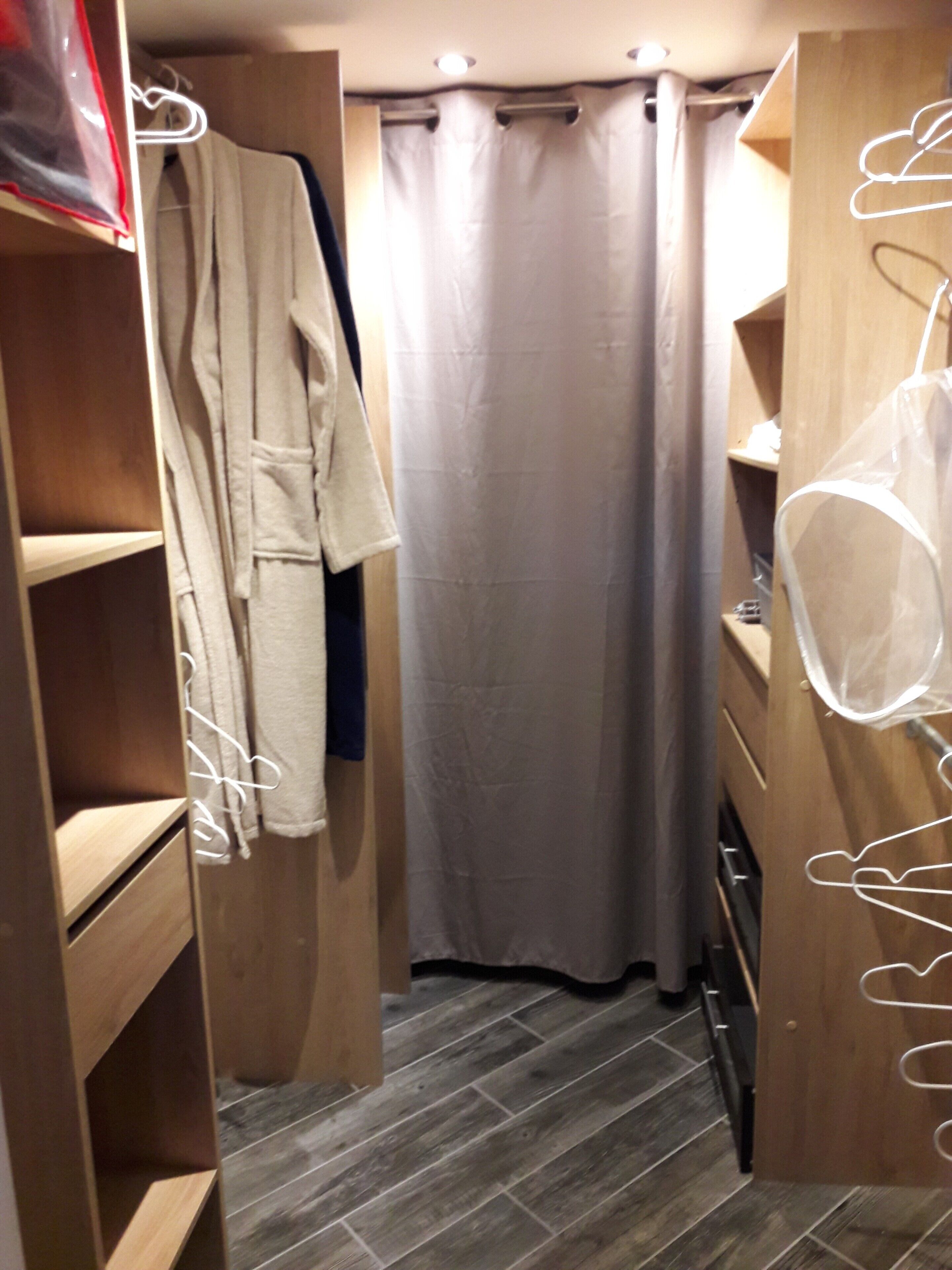 Un dressing avec des étagères en bois, un porte-manteau et un rideau de douche.