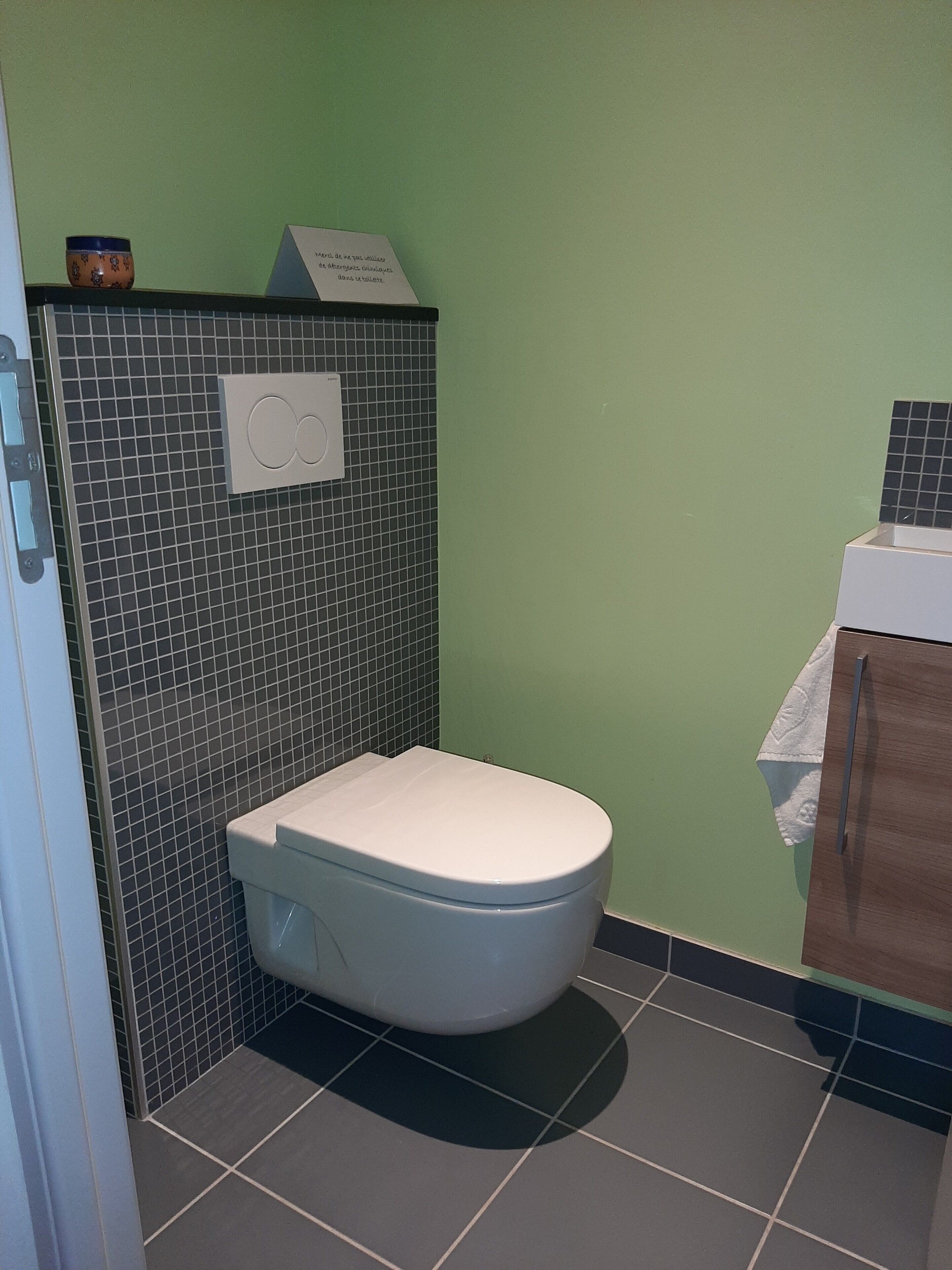 A bathroom with a white toilet, a tiled wall, a small trash bin, and a sign on the wall.
